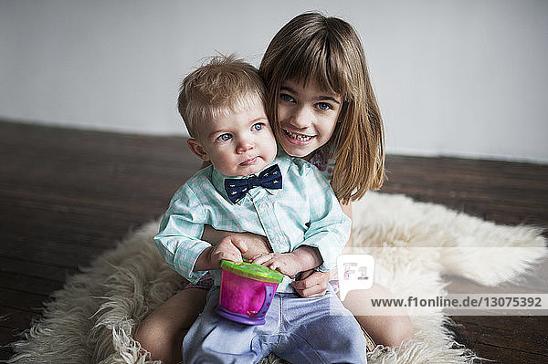 Porträt eines glücklichen Mädchens  das zu Hause mit einem kleinen Jungen auf einem Teppich sitzt