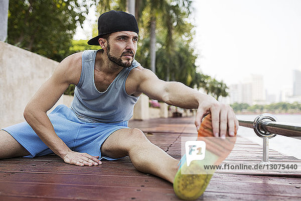 Man sitting and stretching on wooden walkway by river