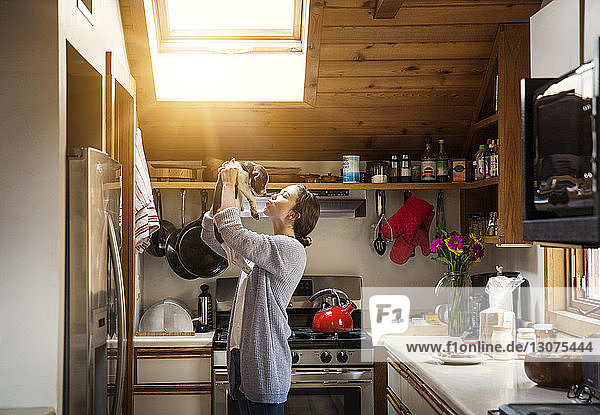 Seitenansicht einer Frau  die mit einem Welpen spielt  während sie zu Hause in der Küche steht