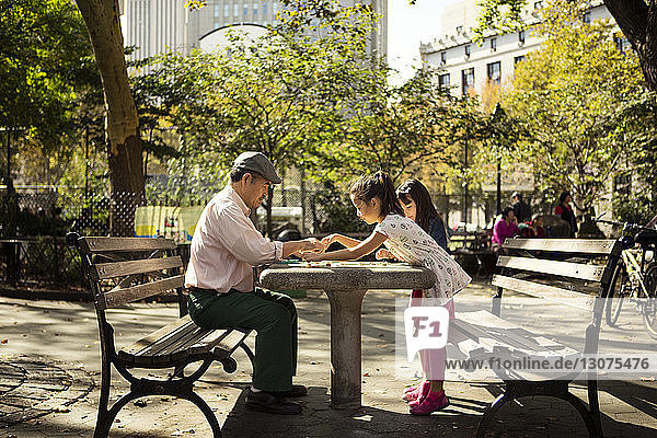 Seitenansicht von Mädchen beim Damespiel mit dem Großvater am Tisch im Park