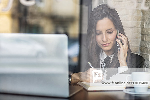 Geschäftsfrau benutzt Smartphone beim Tagebuchschreiben im Café