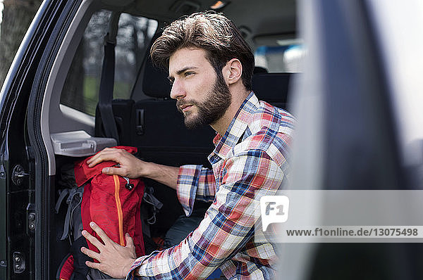 Seitenansicht eines nachdenklichen Mannes  der im Kofferraum eines Autos sitzt