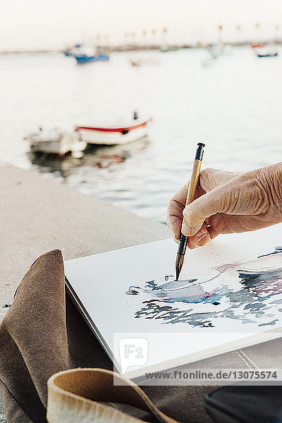 Ausschnitt einer Frau  die auf Papier malt  mit Booten  die auf See festgemacht sind