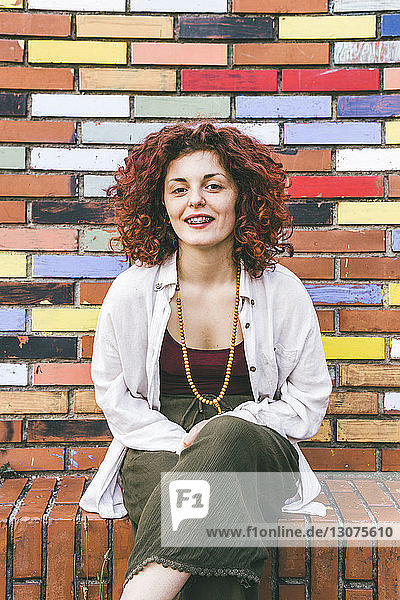 Portrait of woman sitting by colorful brick wall