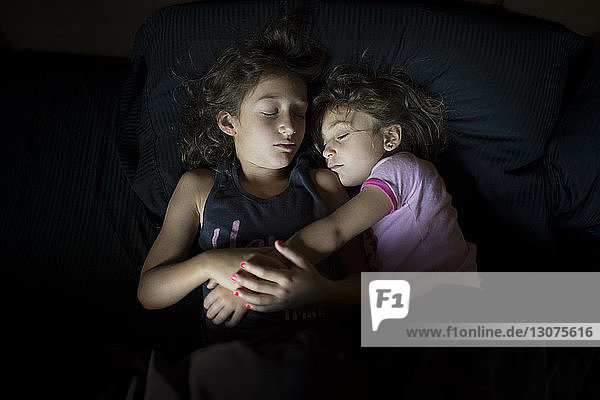 High angle view of sisters sleeping on bed at home