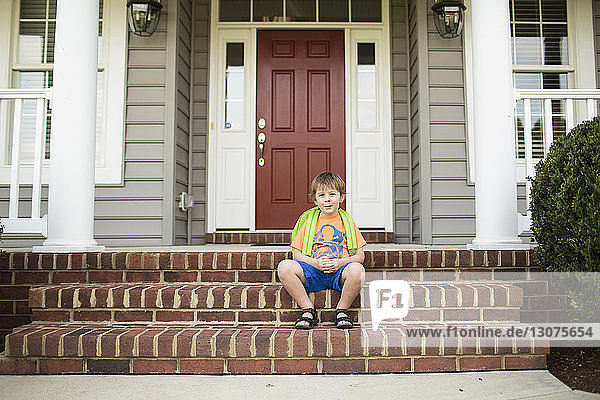Porträt eines Schuljungen  der auf Stufen vor dem Haus sitzt
