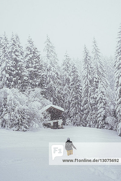 Rückansicht einer Frau  die bei Schneefall auf einem schneebedeckten Berg steht