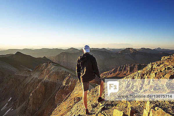 Rückansicht eines Mannes  der auf Berge schaut  während er auf einem Felsen vor klarem Himmel steht