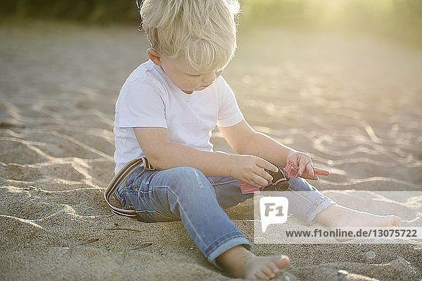 Kleiner Junge spielt mit Spielzeug  während er am Strand im Sand sitzt