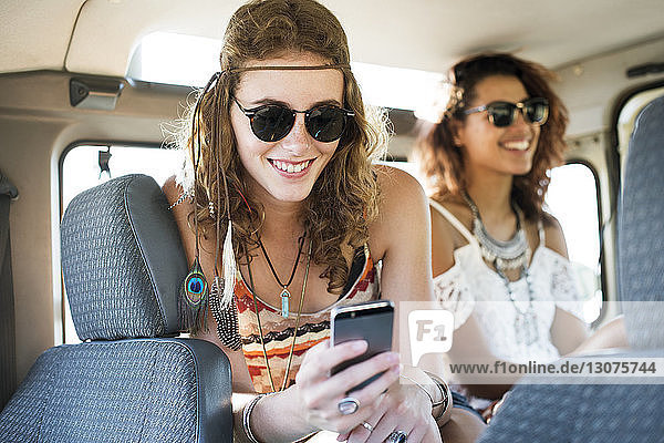Woman using mobile phone while sitting with female friend in off-road vehicle