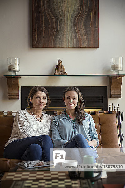 Portrait of smiling daughter and mother sitting on sofa in living room