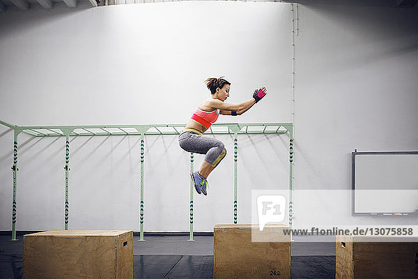 Side view of confident female athlete doing box jumping at gym