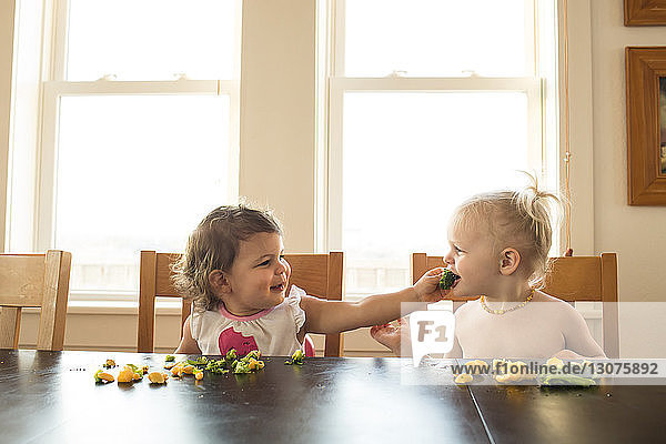 Baby girl feeding food to sister while sitting at table