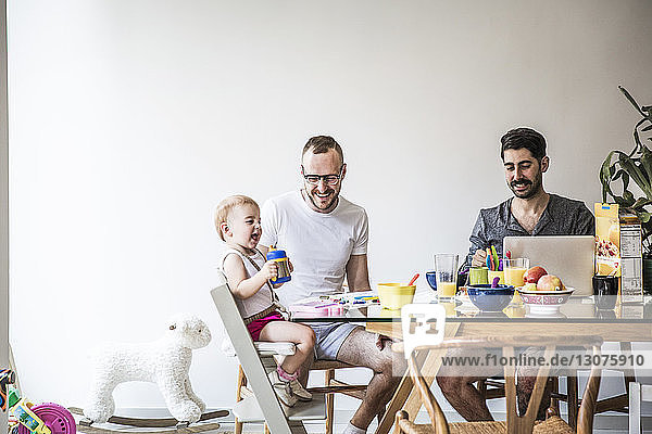 Fathers playing with daughter while having breakfast at table against wall