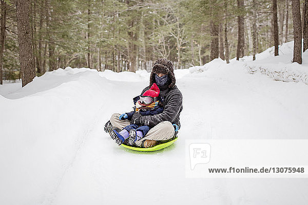 Father sitting with daughter on sled at snow covered field