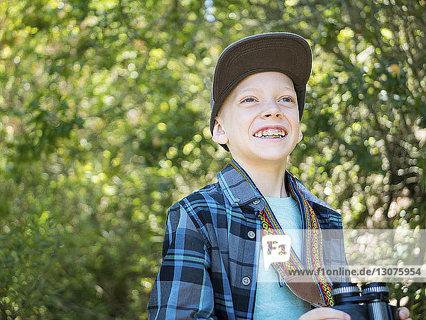 Fröhlicher Junge schaut weg  während er ein Fernglas im Wald hält