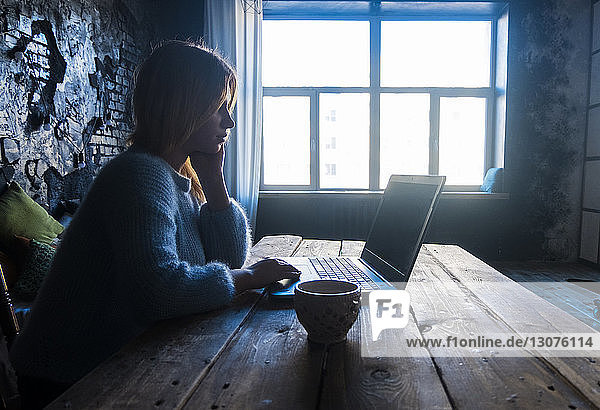 Teenagerin benutzt Laptop-Computer  während sie zu Hause am Tisch sitzt