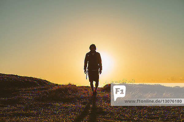 Full length of hiker walking on grassy field against clear sky during sunset