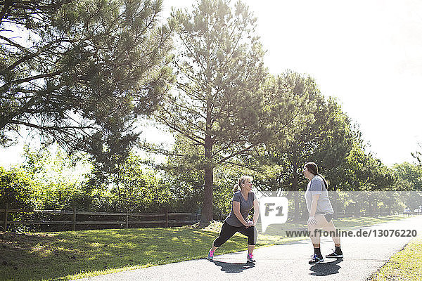 Mutter und Tochter strecken in voller Länge die Beine  während sie auf einem Fußweg im Park trainieren