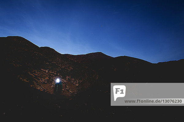 Woman wearing headlamp standing by mountain against blue sky
