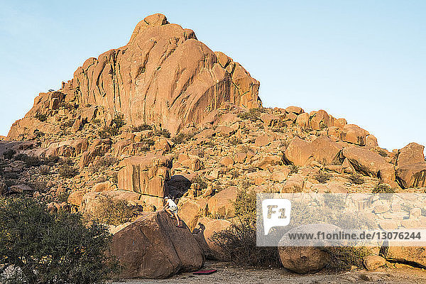 Mann klettert auf Fels gegen Berge und klaren Himmel in der Wüste
