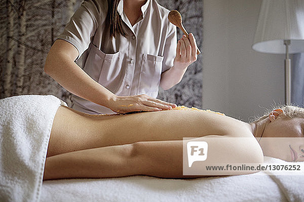 Mittelteil einer Massagetherapeutin  die im Spa Medikamente auf dem Rücken der Frau anwendet