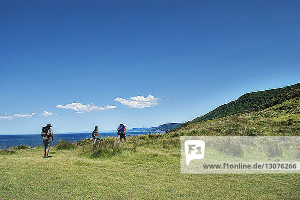 Hikers climbing mountain by sea against blue sky