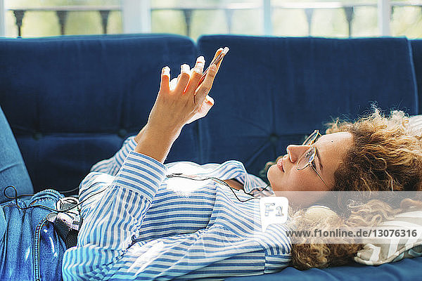 Seitenansicht einer Frau  die ein Smartphone benutzt  während sie zu Hause auf dem Sofa liegt
