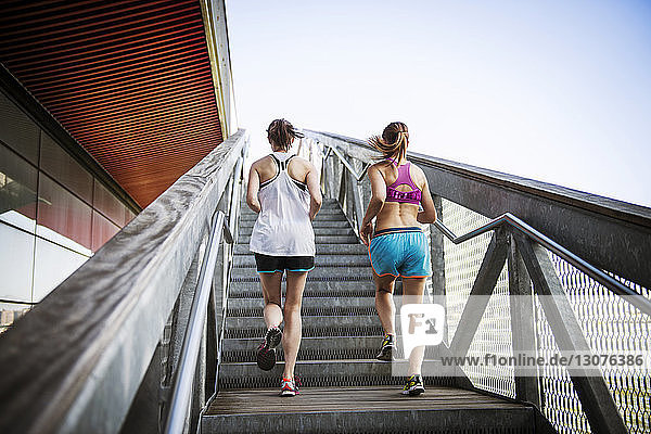 Rückansicht von Frauen  die auf Stufen und Treppen gegen den klaren Himmel joggen