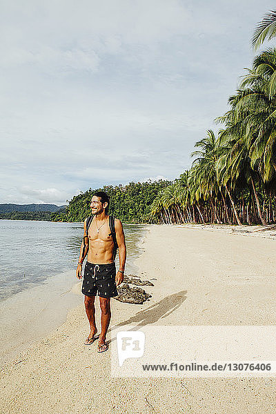 Wanderer ohne Hemd in voller Länge mit Rucksack am Strand stehend
