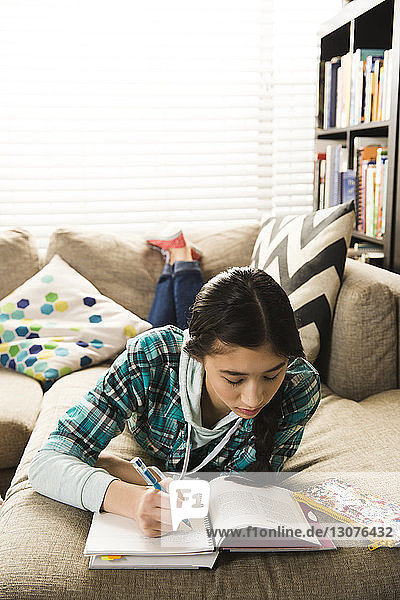 Schwere Teenagerin in voller Länge  die Hausaufgaben macht  während sie zu Hause auf der Couch liegt