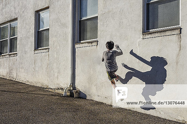Rückansicht eines Teenagers  der an einem sonnigen Tag über eine Mauer springt