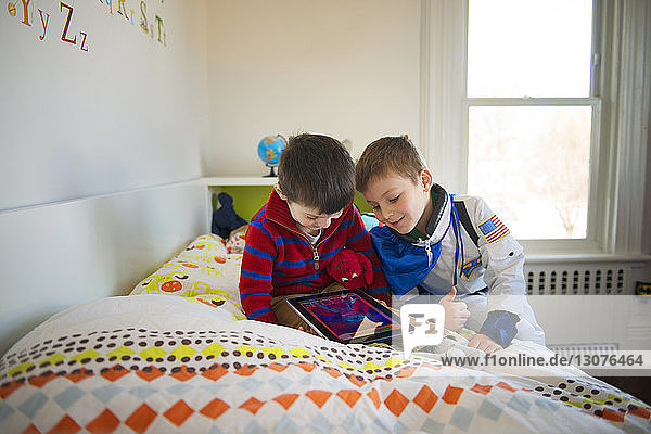 Brothers looking at digital tablet on bed at home