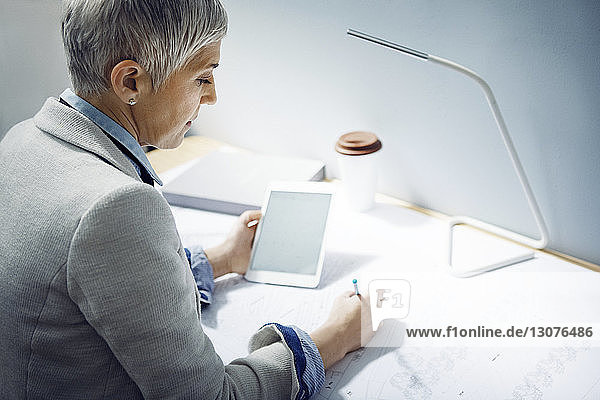 Woman using tablet while writing on paper at table in office