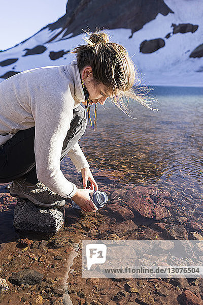 Hochwinkelaufnahme einer Wanderin  die Wasser aus einem Fluss in eine Flasche füllt