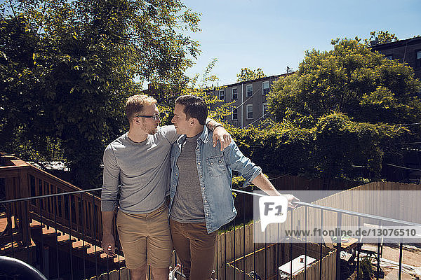 Front view of gay couple standing in balcony against trees