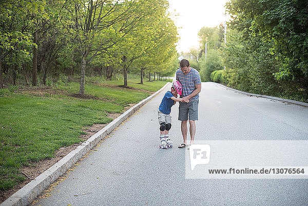 Vater assistiert Sohn beim Rollschuhlaufen auf der Straße im Park