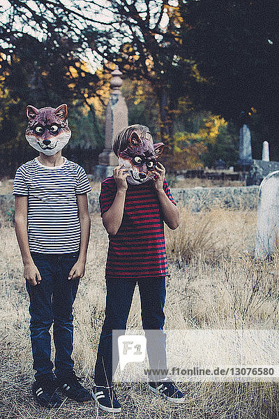 Siblings wearing animal masks while standing at cemetery