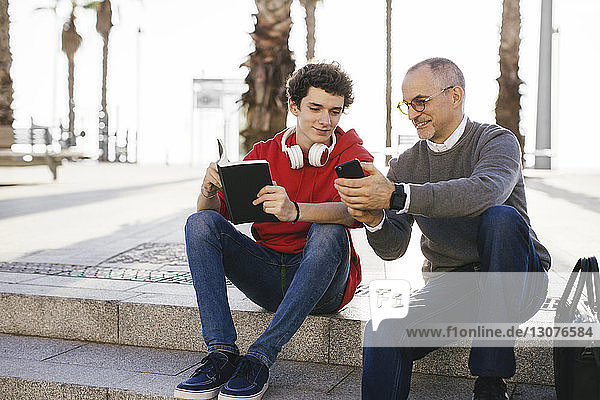 Glücklicher Vater zeigt seinem Sohn ein Smartphone  während er auf einer Treppe in der Stadt sitzt