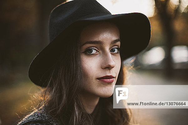 Close-up portrait of woman wearing hat while sitting at park during sunset