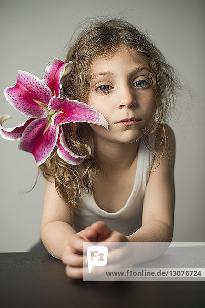 Portrait of girl wearing lily while leaning on table against wall at home
