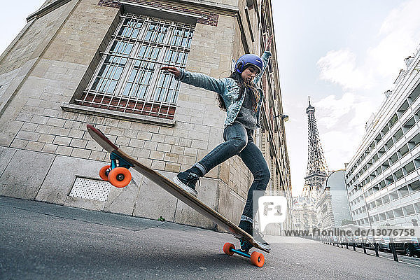 Skateboard fahrende Frau in voller Länge gegen den Eiffelturm