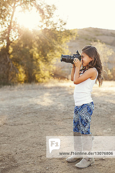Side view of girl standing on field and photographing with camera