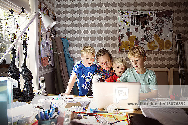 Mutter und Söhne benutzen Laptop auf unordentlichem Tisch an der Wand zu Hause