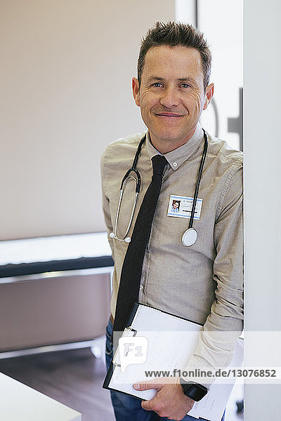 Porträt eines lächelnden Arztes  der im Krankenhaus an der Wand lehnt