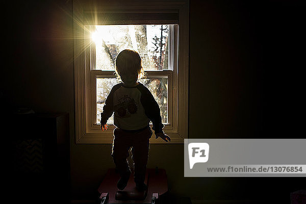 Scherenschnitt-Junge steht zu Hause am Fenster in der Dunkelkammer