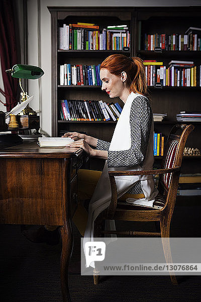 Side view of businesswoman reading book at desk in creative office
