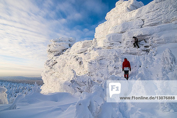 Friends hiking on snow covered mountain against sky