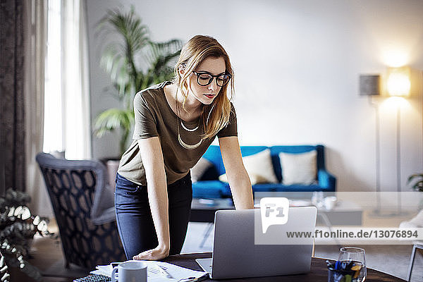 Businesswoman looking at laptop while leaning on table in creative office