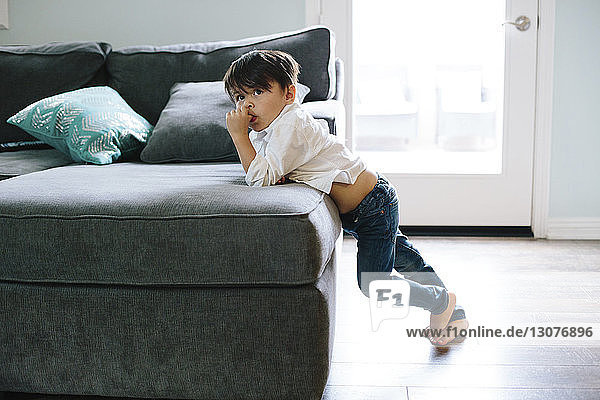 Junge schaut weg  während er sich zu Hause auf das Sofa lehnt